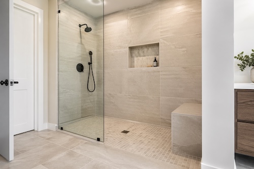 Walk-in shower tile installation in Calgary with large-format wall tile, mosaic shower floor, built-in niche, bench, and frameless glass panel
